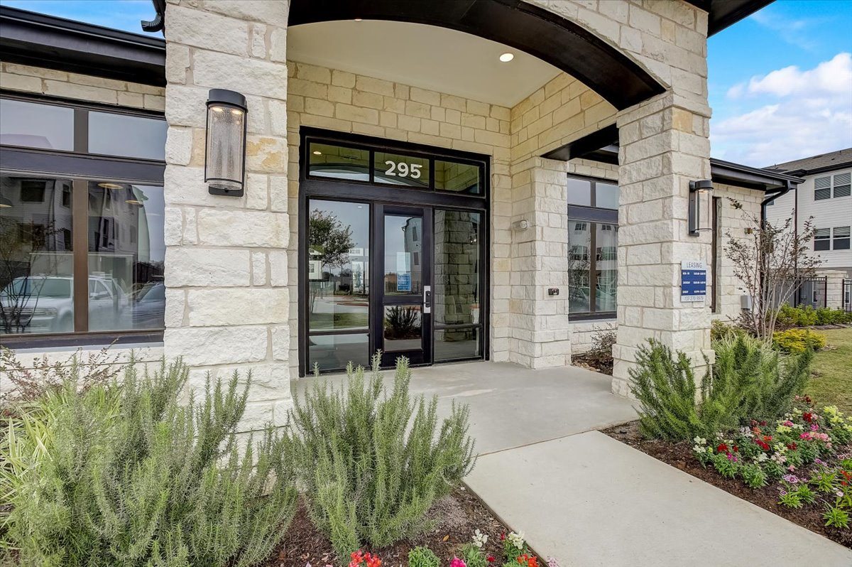 Stone-arched community clubhouse entrance with glass doors, covered entry, and landscaped beds.